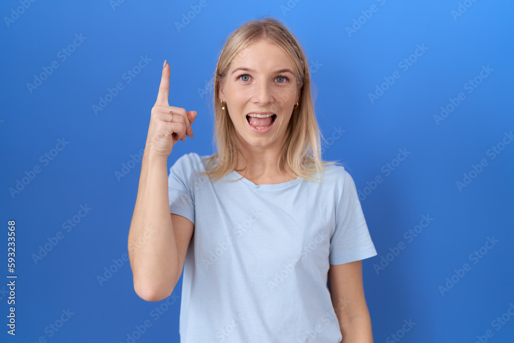 Young caucasian woman wearing casual blue t shirt pointing finger up with successful idea. exited and happy. number one. Young caucasian woman wearing casual blue t shirt pointing finger up with successful idea. exited and happy. number one.