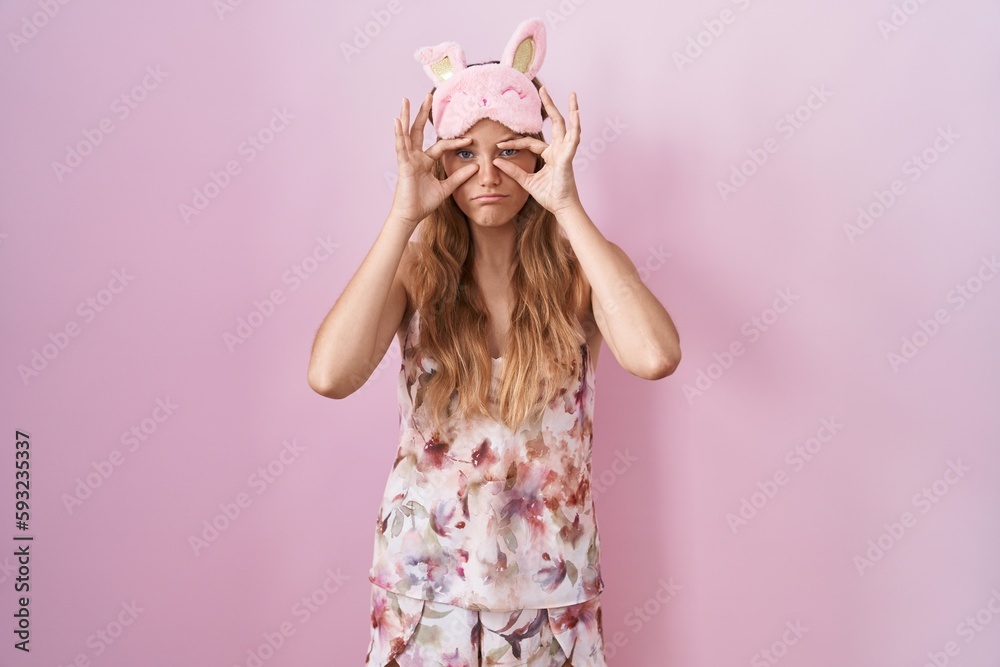 Young caucasian woman wearing sleep mask and pajama trying to open eyes with fingers, sleepy and tired for morning fatigue Young caucasian woman wearing sleep mask and pajama trying to open eyes with fingers, sleepy and tired for morning fatigue