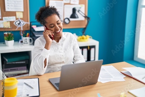 African american woman business worker using laptop talking on smartphone at office