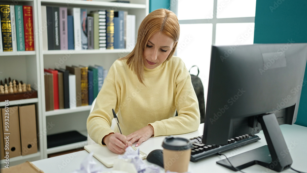 Young blonde woman student using computer writing on notebook at university classroom Young blonde woman student using computer writing on notebook at university classroom