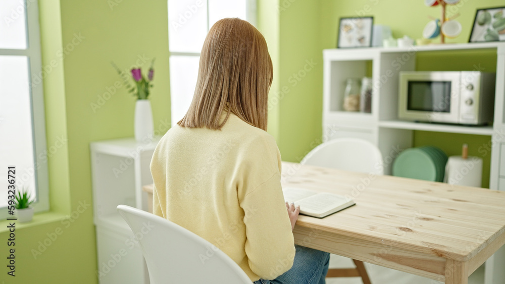 Young blonde woman reading book sitting on table at home Young blonde woman reading book sitting on table at home