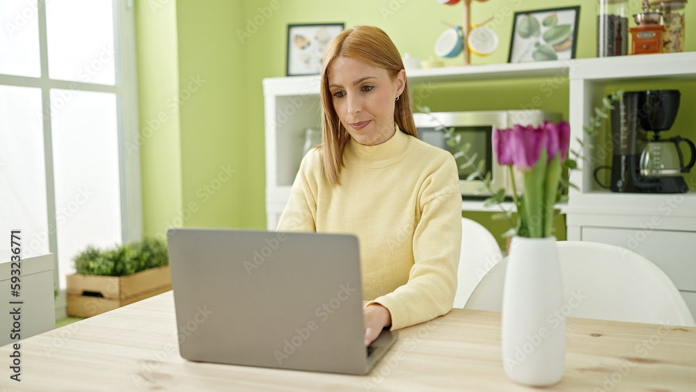 Young blonde woman using laptop sitting on table at home