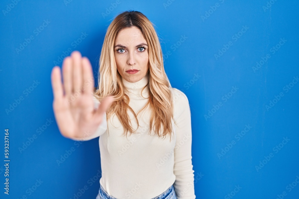 Fototapeta premium Young caucasian woman standing over blue background doing stop sing with palm of the hand. warning expression with negative and serious gesture on the face.
