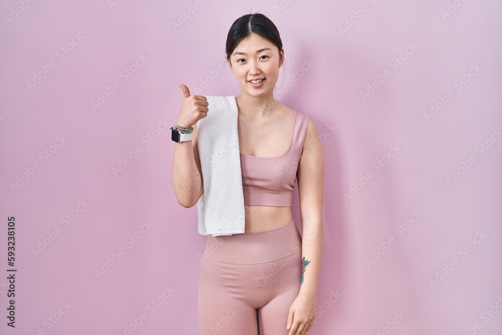 Chinese young woman wearing sportswear and towel doing happy thumbs up gesture with hand. approving expression looking at the camera showing success. Chinese young woman wearing sportswear and towel doing happy thumbs up gesture with hand. approving expression looking at the camera showing success.