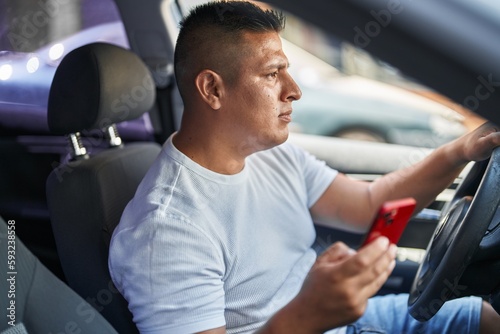 Young latin man using smartphone sitting on car at street
