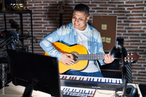 Hispanic young man playing classic guitar at music studio with a happy and cool smile on face. lucky person.