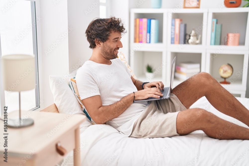 Young hispanic man using laptop sitting on bed at bedroom Young hispanic man using laptop sitting on bed at bedroom