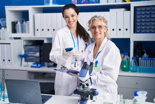 Two women scientists using smartphone working at laboratory