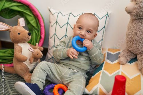 Adorable caucasian baby sitting on floor sucking hoops at home