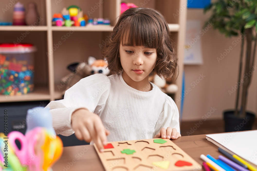 Fototapeta premium Adorable hispanic girl playing with maths puzzle game sitting on table at kindergarten