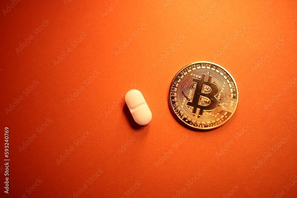 Top view of a golden Bitcoin coin and a pill on an orange background - the concept of cryptocurrency Top view of a golden Bitcoin coin and a pill on an orange background - the concept of cryptocurrency
