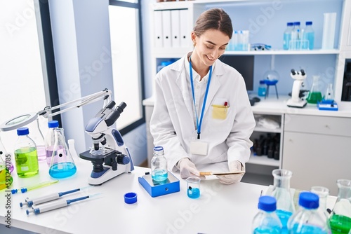 Young caucasian woman scientist weighing liquid reading notebook at laboratory
