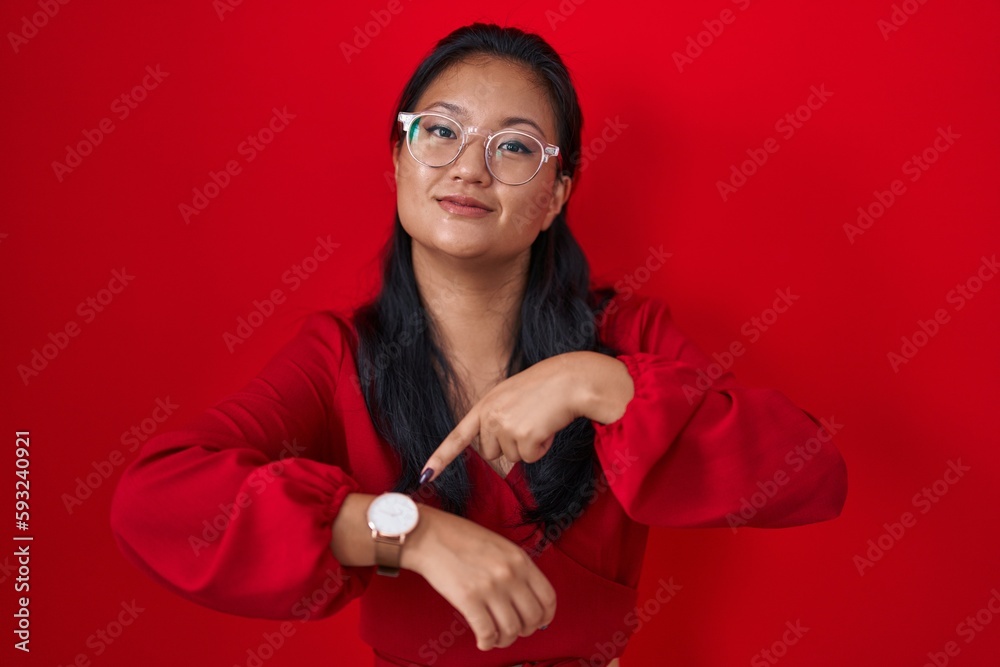 Asian young woman standing over red background in hurry pointing to watch time, impatience, upset and angry for deadline delay Asian young woman standing over red background in hurry pointing to watch time, impatience, upset and angry for deadline delay