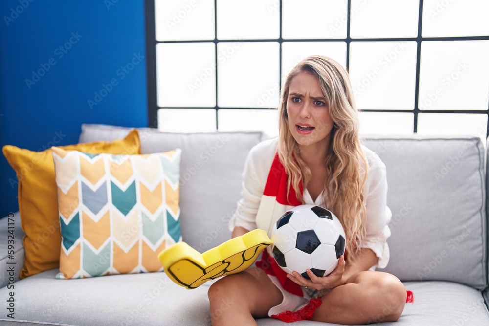 Young blonde woman supporting soccer team sitting on sofa at home Young blonde woman supporting soccer team sitting on sofa at home