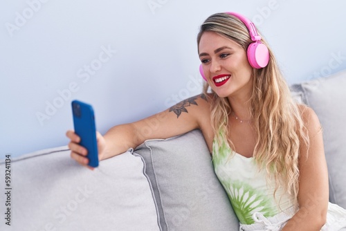 Young beautiful hispanic woman listening to music sitting on sofa at home