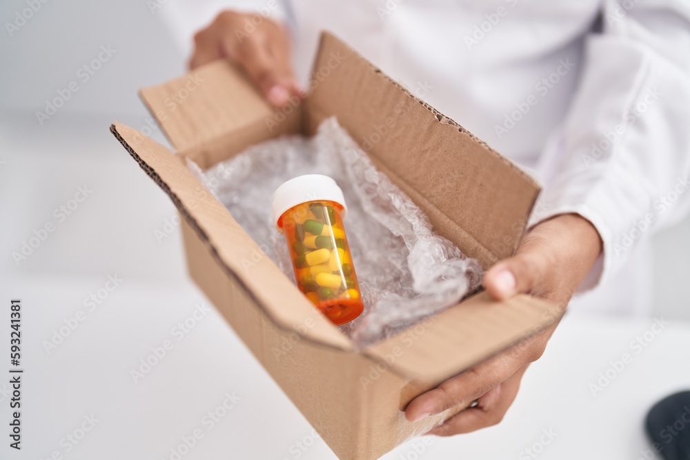 Young hispanic woman pharmacist holding package with capsule bottle at pharmacy