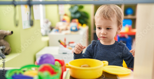 Adorable blond toddler playing with play kitchen standing at kindergarten