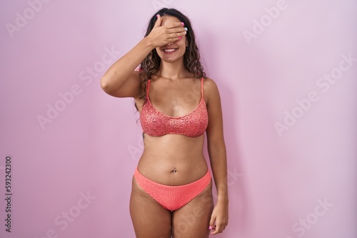 Young hispanic woman wearing lingerie over pink background smiling and laughing with hand on face covering eyes for surprise. blind concept.