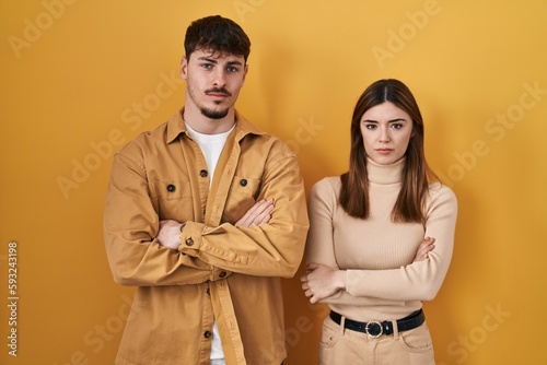 Young hispanic couple standing over yellow background skeptic and nervous, disapproving expression on face with crossed arms. negative person. © Krakenimages.com