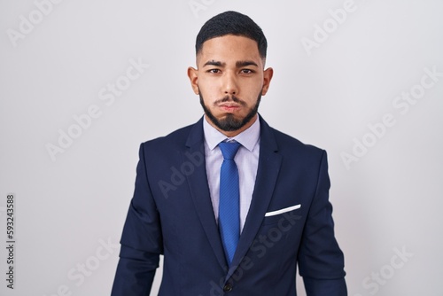 Young hispanic man wearing business suit and tie puffing cheeks with funny face. mouth inflated with air, crazy expression.