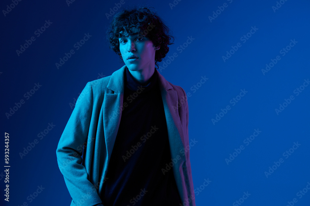 Male model in fashion coat on dark blue background, neon light, style and trends, mixed light, men's fashion Male model in fashion coat on dark blue background, neon light, style and trends, mixed light, men's fashion