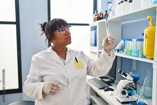 Young beautiful latin woman scientist looking test tube with plant at laboratory