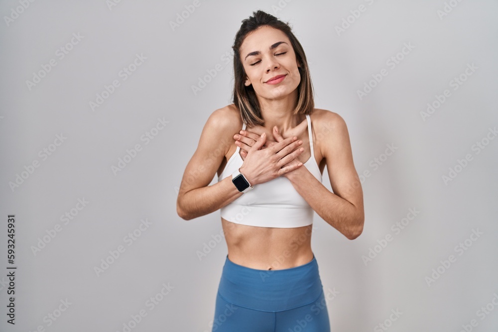 Hispanic woman wearing sportswear over isolated background smiling with hands on chest with closed eyes and grateful gesture on face. health concept.