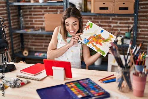 Young beautiful hispanic woman artist having video call shwowing draw at art studio photo