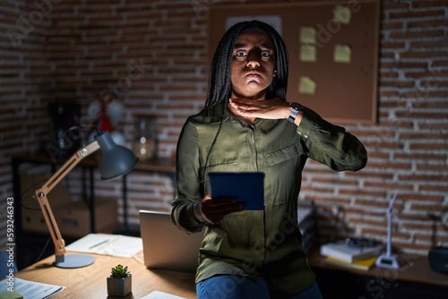 Young african american with braids working at the office at night cutting throat with hand as knife, threaten aggression with furious violence photo
