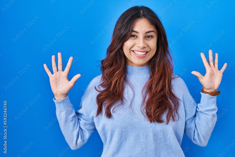 Hispanic young woman standing over blue background showing and pointing up with fingers number ten while smiling confident and happy. Hispanic young woman standing over blue background showing and pointing up with fingers number ten while smiling confident and happy.