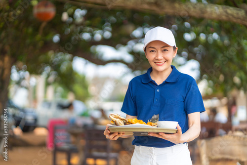 Portrait of Asian woman waiter serving food and drink to customer on the table at tropical beach cafe and restaurant on summer holiday vacation. Food and drink business service occupation concept. photo