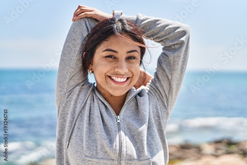 Young hispanic woman stretching arms training at seaside photo