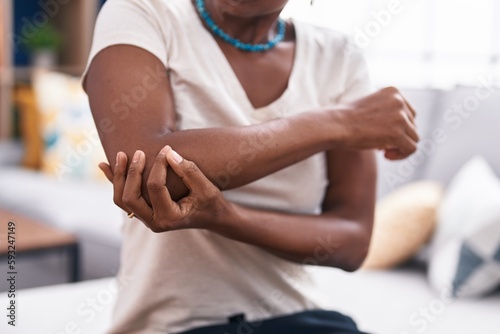 Middle age african american woman sitting on sofa suffering for elbow pain at home