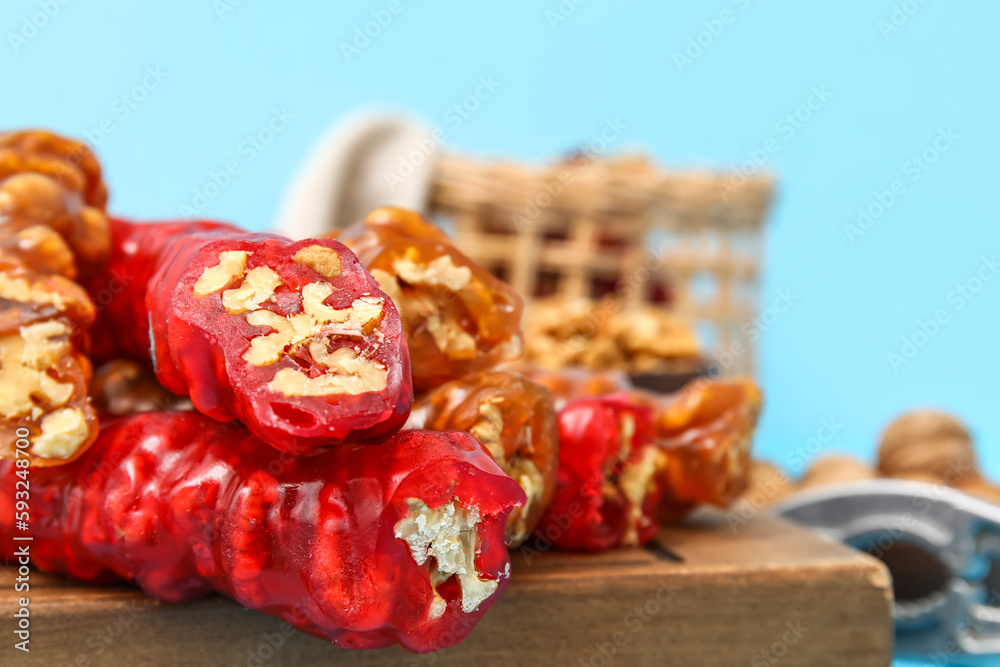 Board with delicious churchkhela and walnuts on blue background