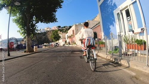 Happy young woman cycling on vintage bike through colorful traditional old town in Ponza island Italy. Fashion dress colorful skirt