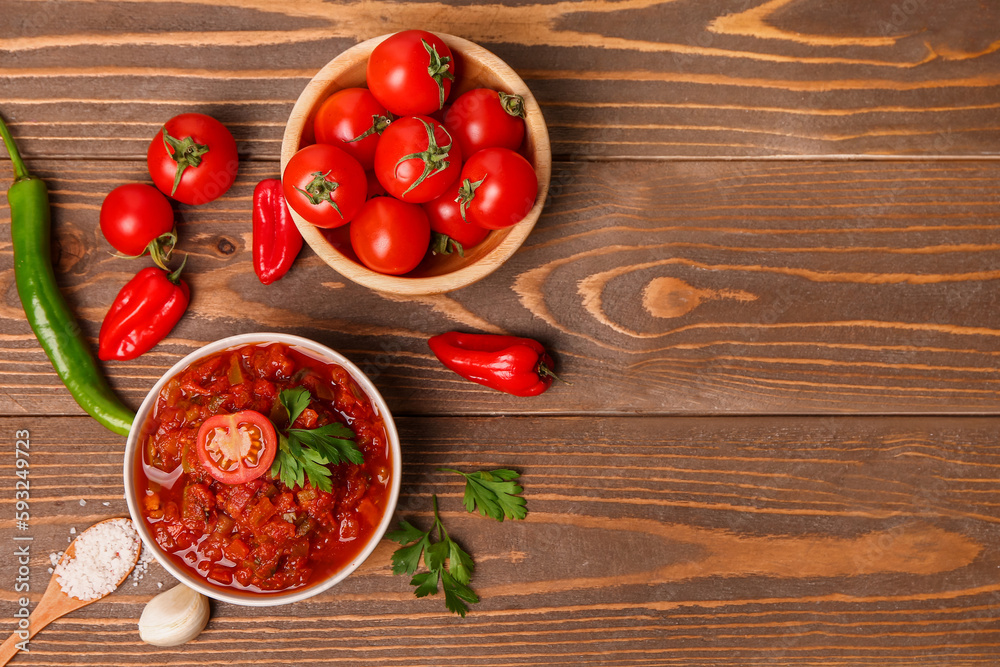 Composition with bowl of delicious salsa sauce and ingredients on brown wooden table Composition with bowl of delicious salsa sauce and ingredients on brown wooden table