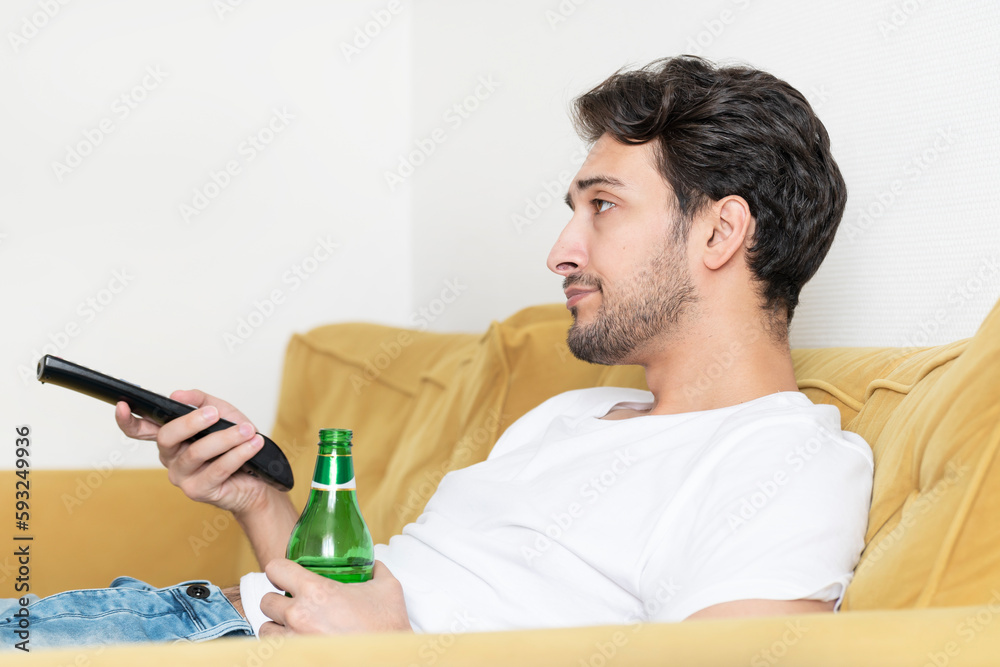 Handsome man lying on the couch and watching tv and drinking beer Handsome man lying on the couch and watching tv and drinking beer