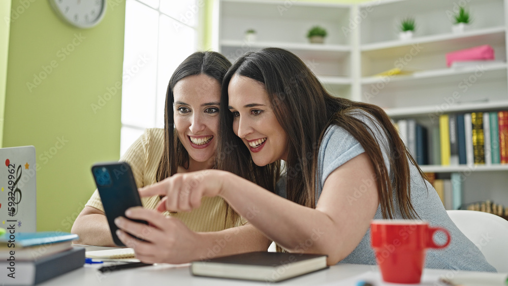 Two women sitting on table studying using smartphone at library university Two women sitting on table studying using smartphone at library university