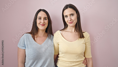 Two women smiling confident hugging each other over isolated pink background