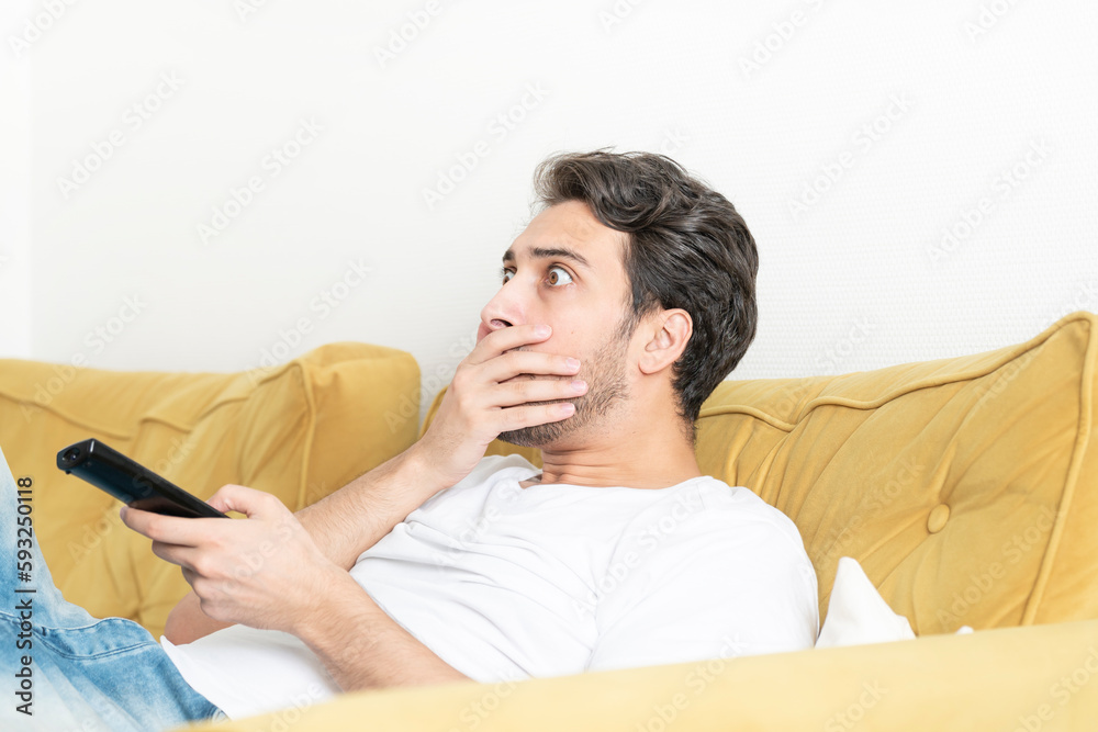 Shocked man sitting on the couch and watching tv at home	