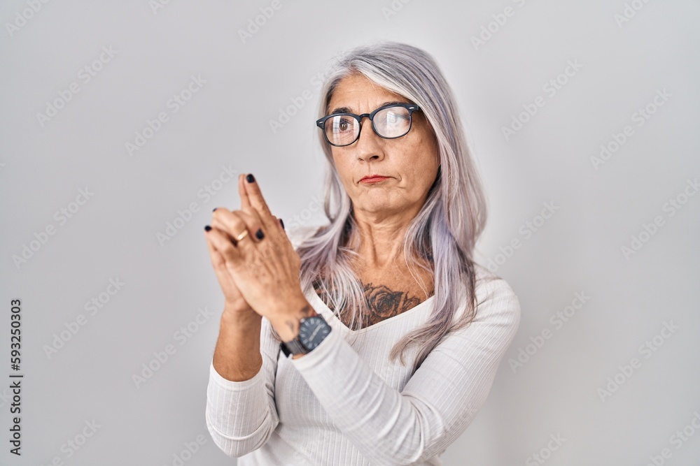 Middle age woman with grey hair standing over white background holding symbolic gun with hand gesture, playing killing shooting weapons, angry face Middle age woman with grey hair standing over white background holding symbolic gun with hand gesture, playing killing shooting weapons, angry face