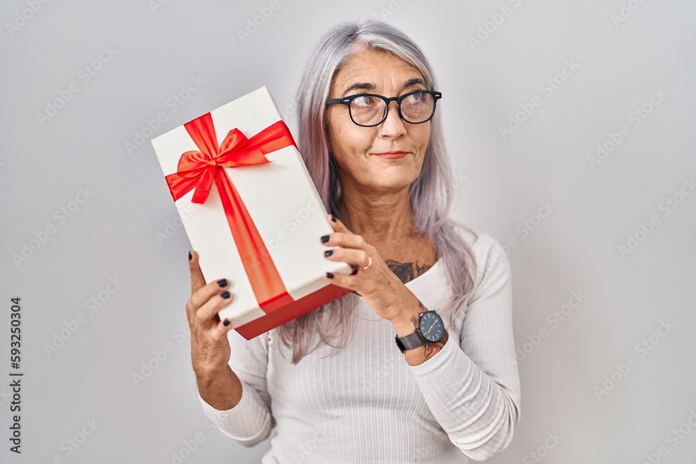 Middle age woman with grey hair holding gift smiling looking to the side and staring away thinking. Middle age woman with grey hair holding gift smiling looking to the side and staring away thinking.