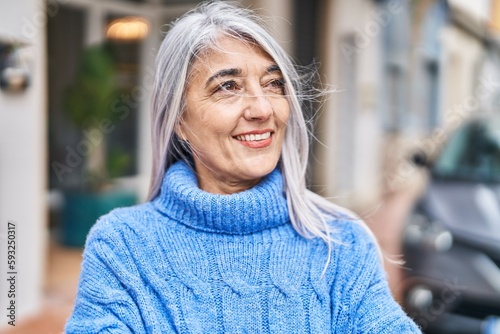 Middle age grey-haired woman smiling confident looking to the side at street