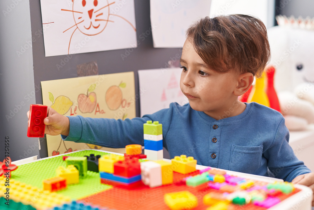 Adorable hispanic boy playing with construction blocks sitting on table at kindergarten Adorable hispanic boy playing with construction blocks sitting on table at kindergarten