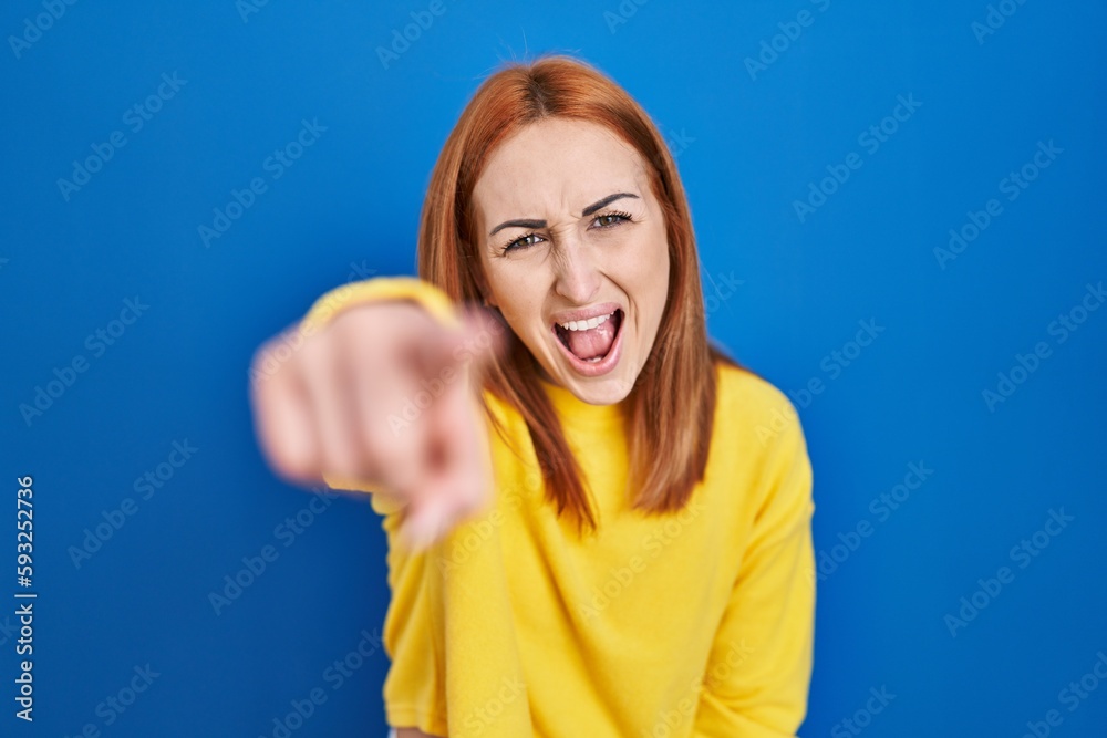 Fototapeta premium Young woman standing over blue background pointing displeased and frustrated to the camera, angry and furious with you