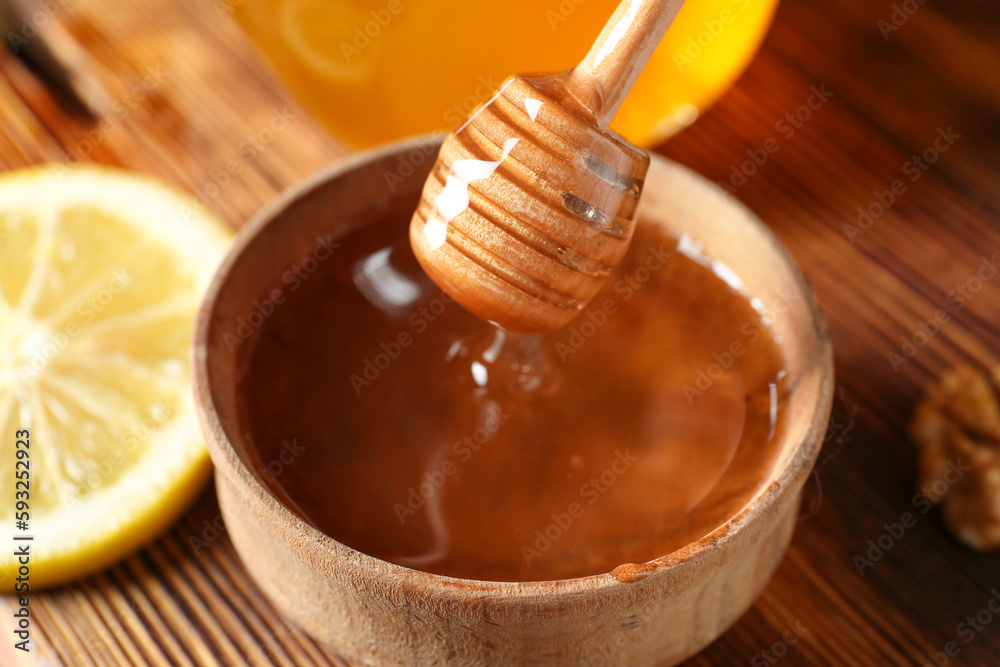 Pouring of sweet honey from dipper into bowl on wooden background, closeup Pouring of sweet honey from dipper into bowl on wooden background, closeup