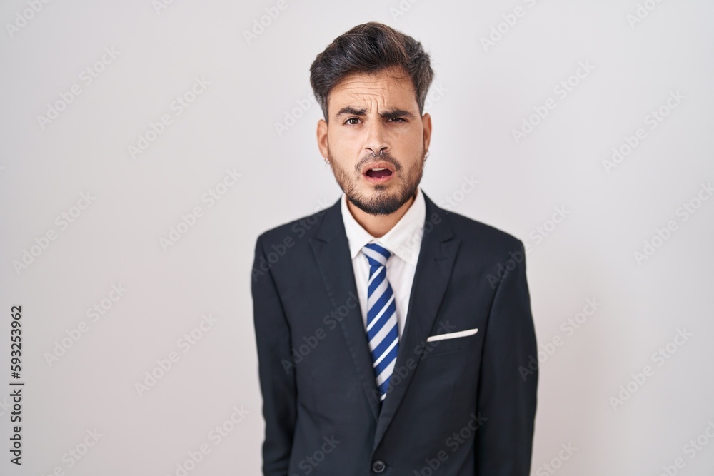 Young hispanic man with tattoos wearing business suit and tie in shock face, looking skeptical and sarcastic, surprised with open mouth Young hispanic man with tattoos wearing business suit and tie in shock face, looking skeptical and sarcastic, surprised with open mouth