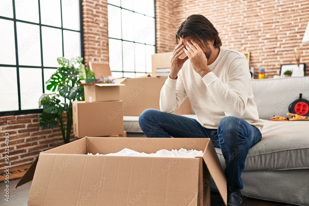 Middle age man unpacking cardboard box with worried expression at new home Middle age man unpacking cardboard box with worried expression at new home