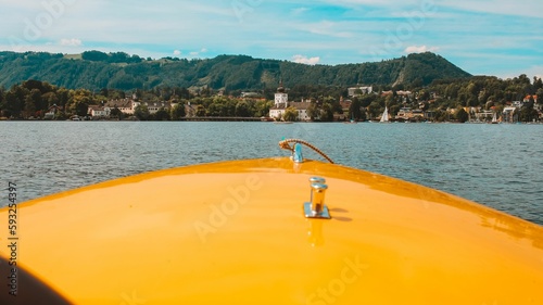 Front of a yellow boat swimming in the waters of lake Traunsee with Gmunden town in the background © Milan Dokic/Wirestock Creators