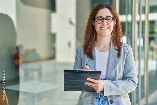 Young woman business worker smiling confident writing on document at street